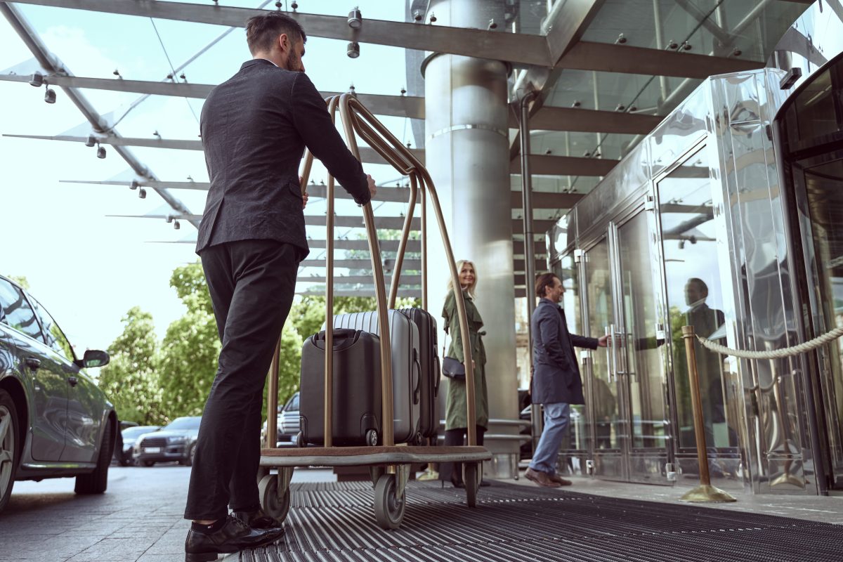 Couple of travellers proceeding inside of the hotel for a check-in while having their luggage deliverd by a porter