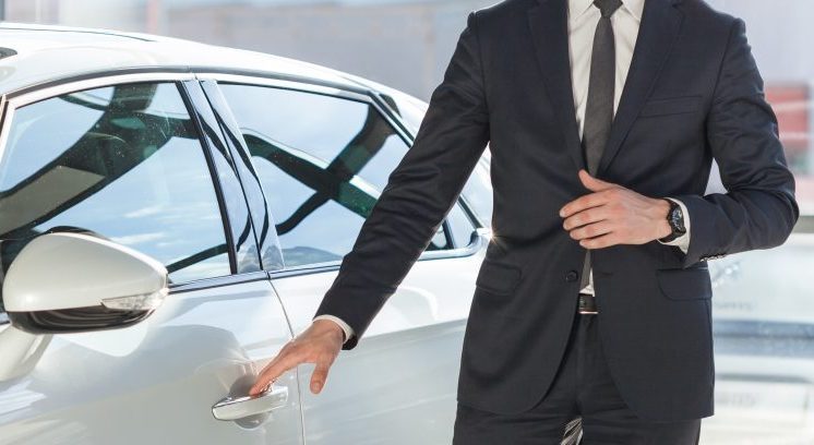 Young man in suit standing by his modern luxurious car